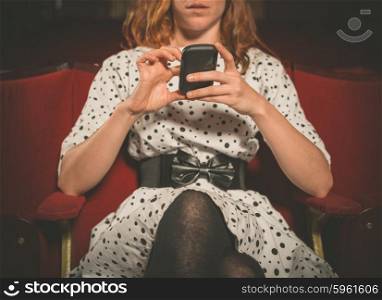 A young woman is sitting on the front row in a movie theater and is using her phone