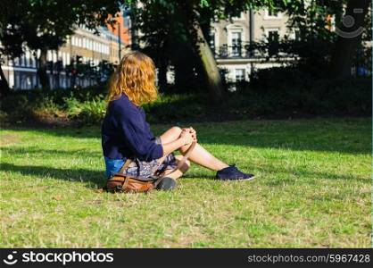 A young woman is sitting on the grass in a park in the city on a sunny summer day