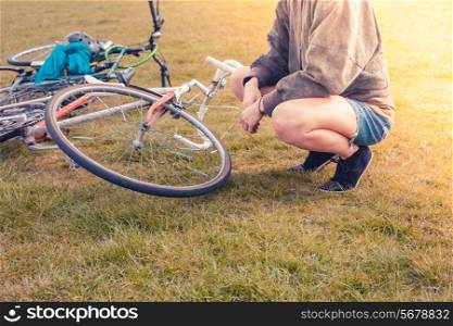 A young woman is sitting on the grass in the park and looking at her bicycle