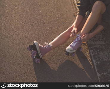 A young woman is sitting on the ground and is putting on roller skates in the park at sunset