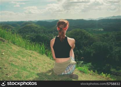 A young woman is sitting on the hillside and is admiring the view of the chocolate hills in Bohol, Philippines