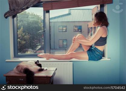 A young woman is sitting on the window sill with a cat next to her