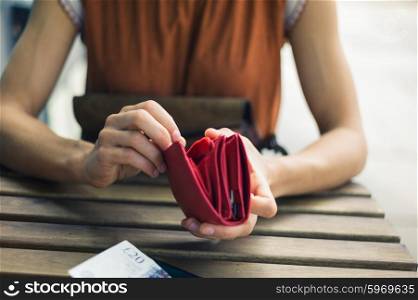 A young woman is sitting outside and is opening her purse to get some cash for paying her bill at a cafe