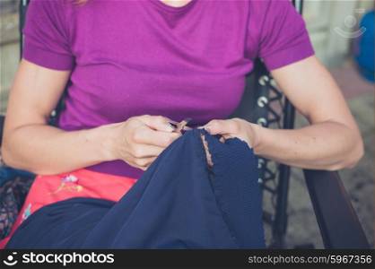A young woman is sitting outside and is sewing a piece of clothing