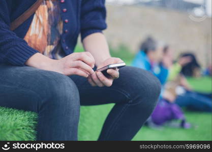 A young woman is sitting outside on some astro turf and is using a smart phone