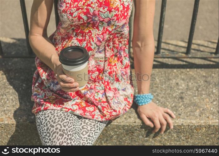 A young woman is sitting outside with a paper cup of coffee