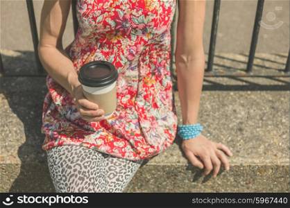 A young woman is sitting outside with a paper cup of coffee