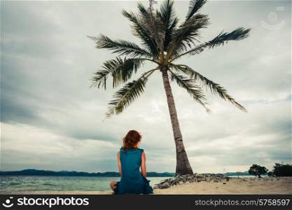 A young woman is sitting under a palm tree on a tropical beach