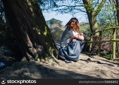 A young woman is sitting under a tree by the water in a forest