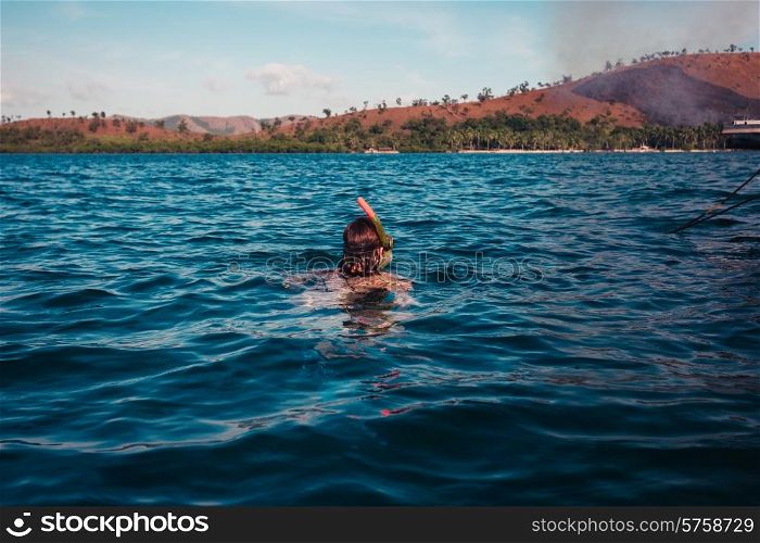 A young woman is snorkeling near a tropical island where there is a fire
