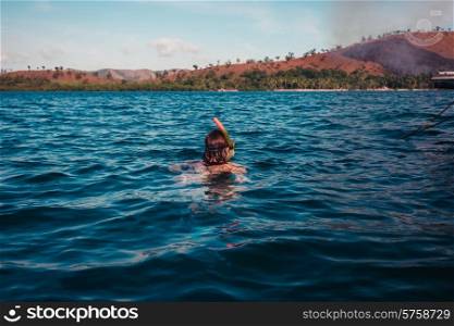 A young woman is snorkeling near a tropical island where there is a fire