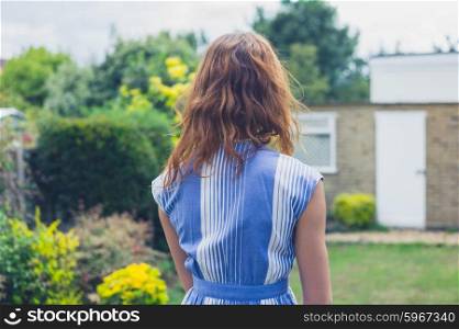 A young woman is standing and relaxing in a residential garden on a sunny summer day