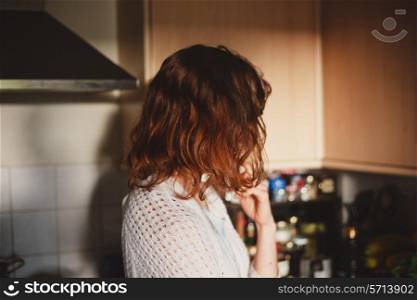 A young woman is standing at home in her kitchen and thinking