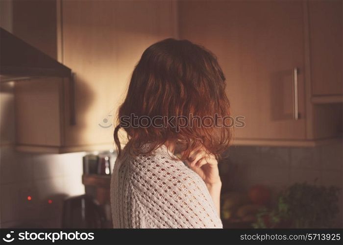 A young woman is standing at home in her kitchen and thinking