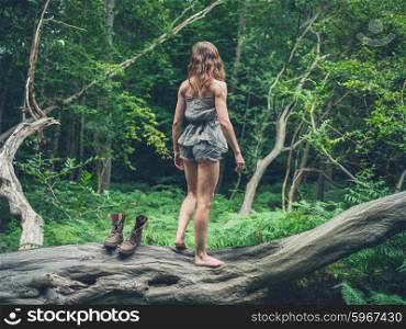 A young woman is standing barefoot on a fallen tree in the forest after having taken off her shoes
