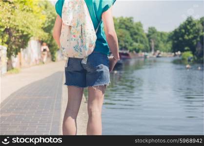 A young woman is standing by a canal in the city on a summer day