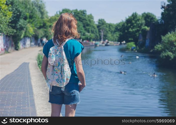A young woman is standing by a canal in the city on a summer day