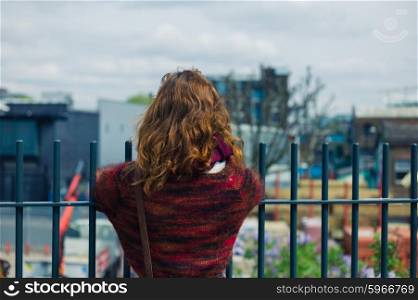 A young woman is standing by a fence and is looking at a builders yard