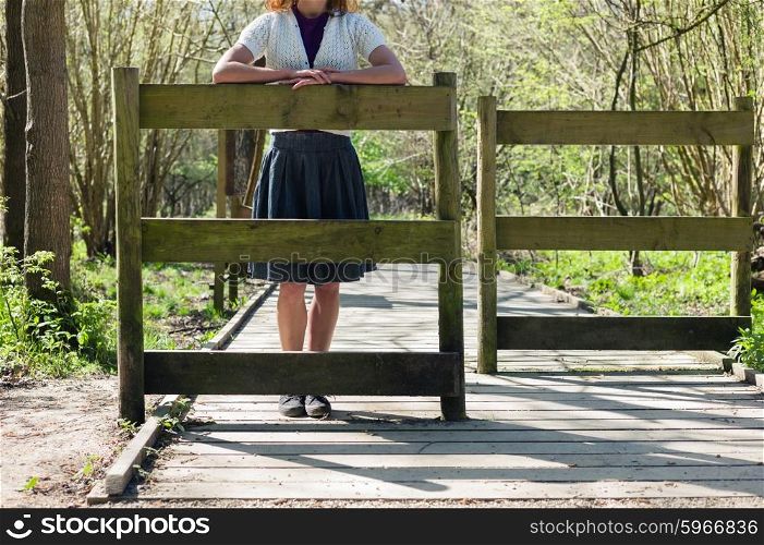 A young woman is standing by a gate in the forest