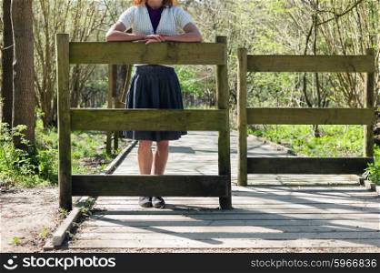 A young woman is standing by a gate in the forest