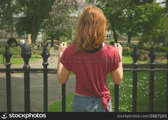 A young woman is standing by a gate outside a park in summer
