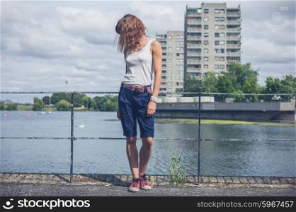A young woman is standing by a marina in an urban area with old concrete tower blocks in the background