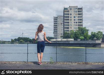 A young woman is standing by a marina in an urban area with old concrete tower blocks in the background