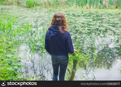A young woman is standing by a pond in a forest
