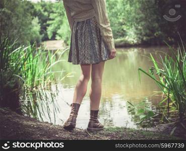 A young woman is standing by a pond in the forest on a sunny day