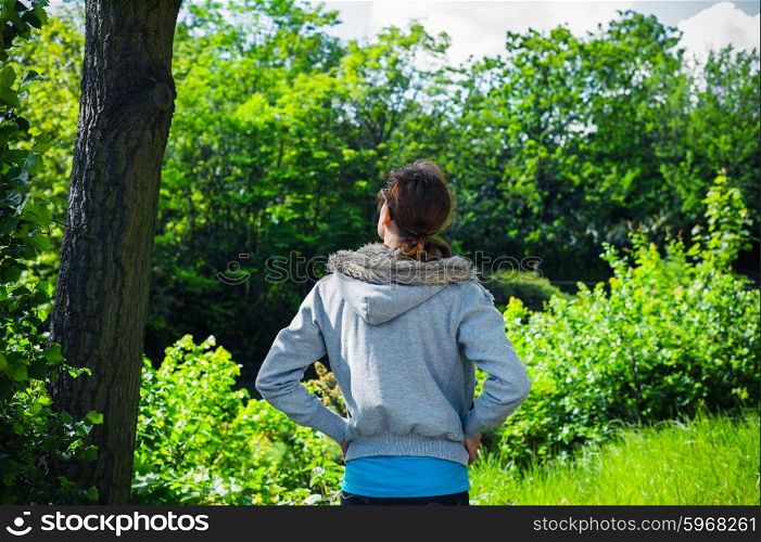 A young woman is standing by a tree in a park on a sunny day