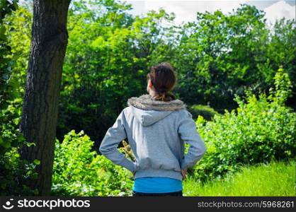 A young woman is standing by a tree in a park on a sunny day