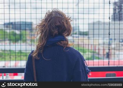 A young woman is standing by a wire fence in the city