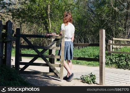 A young woman is standing by a wooden gate in a forest