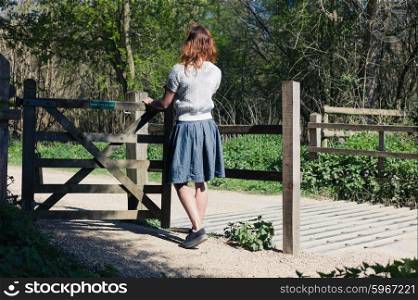 A young woman is standing by a wooden gate in a forest
