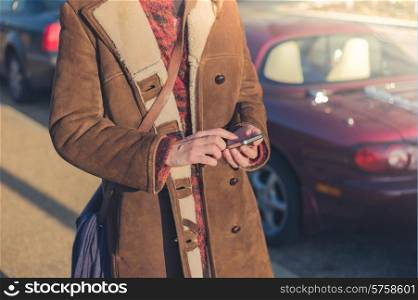 A young woman is standing by her fancy car and is using her smart phone in winter