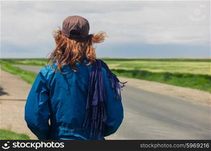 A young woman is standing by the roadside in the country and is looking at a gloomy sky