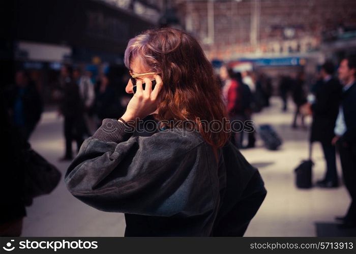 A young woman is standing in a busy station and talking on the phone