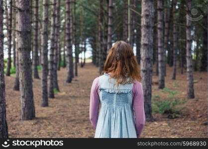 A young woman is standing in a clearing in the forest and is looking at the trees