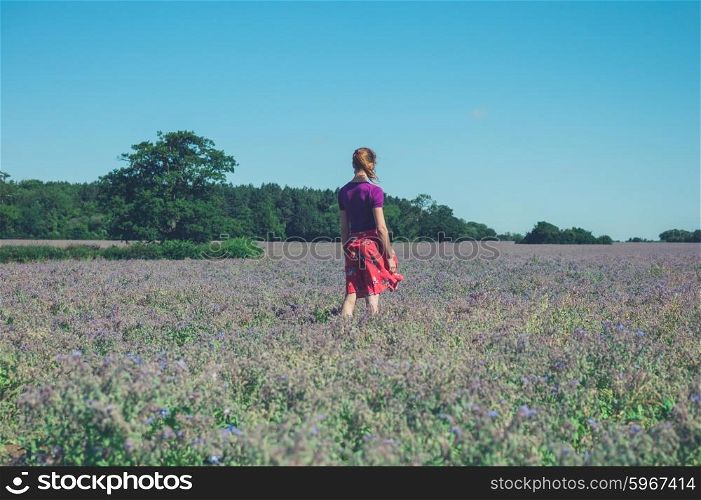 A young woman is standing in a field of purple flowers on a sunny summer day