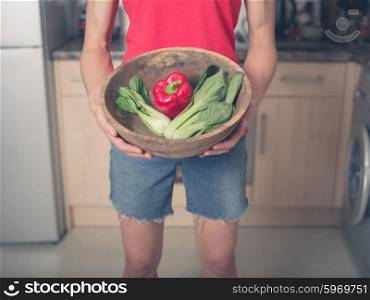 A young woman is standing in a kitchen with a bowl of pak choi and red pepper