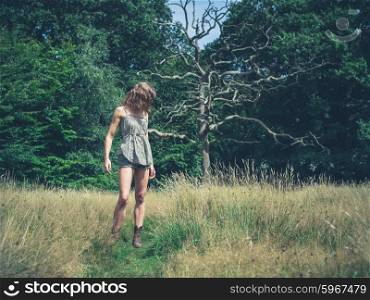 A young woman is standing in a meadow by a clearing of the forest on a sunny summer day