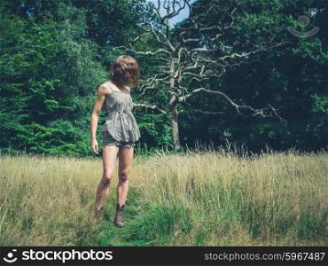 A young woman is standing in a meadow by a clearing of the forest on a sunny summer day