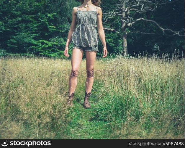 A young woman is standing in a meadow by a clearing of the forest on a sunny summer day