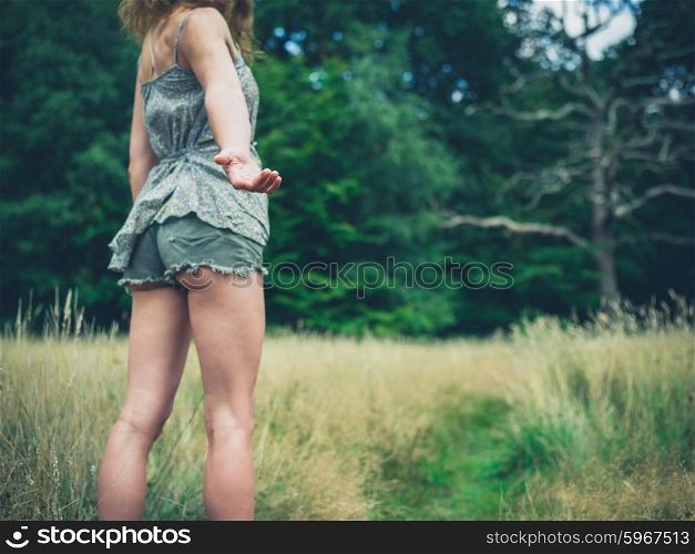 A young woman is standing in a meadow in the forest on a sunny summer day and is offering a helping hand