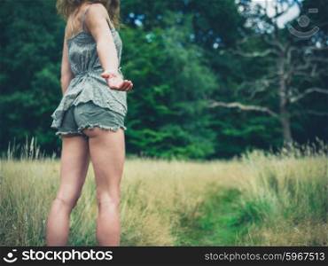 A young woman is standing in a meadow in the forest on a sunny summer day and is offering a helping hand