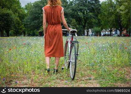 A young woman is standing in a meadow with a bicycle