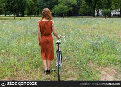 A young woman is standing in a meadow with a bicycle