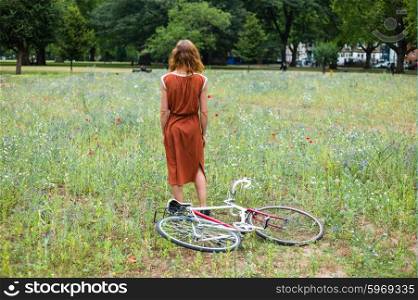 A young woman is standing in a meadow with a bicycle on the ground next to her