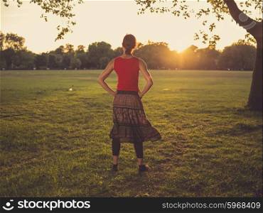 A young woman is standing in a park and is admiring the sunset
