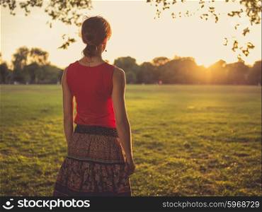 A young woman is standing in a park and is admiring the sunset
